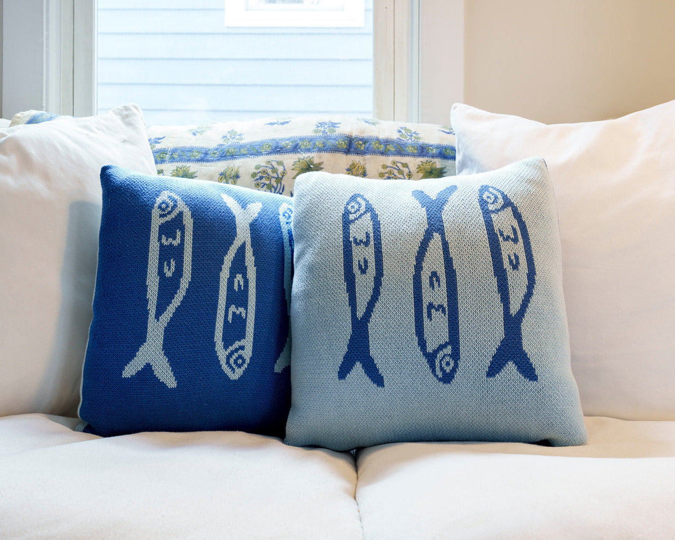 Two decorative pillows with fish patterns on a white couch.