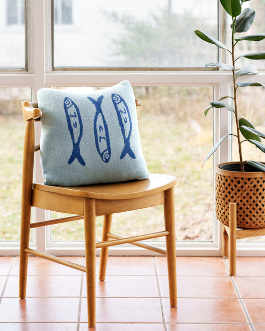 Decorative pillow with fish pattern on a wooden chair near a window with a plant in the background